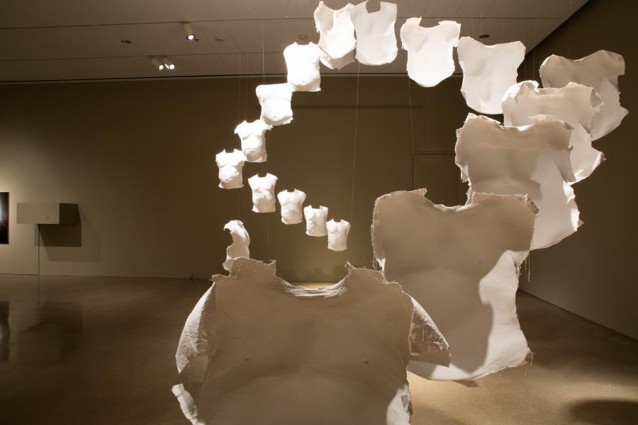 A close-up view of a suspended installation of cast torso forms, highlighting their textured surfaces and shadow play in the gallery lighting.