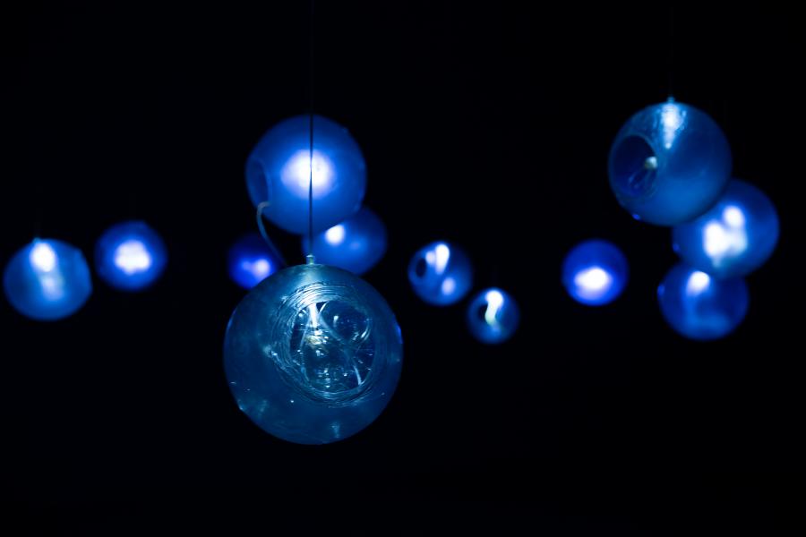 Multiple glowing blue glass orbs suspended in a dark gallery space, their soft blue light creating a mesmerizing ambiance.