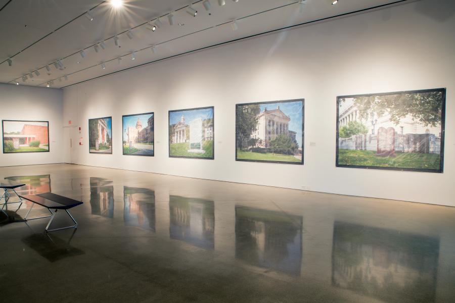 Gallery installation view featuring large-scale photographs of various courthouse buildings displayed on white walls, with polished concrete floors reflecting the artworks and benches arranged for viewers.