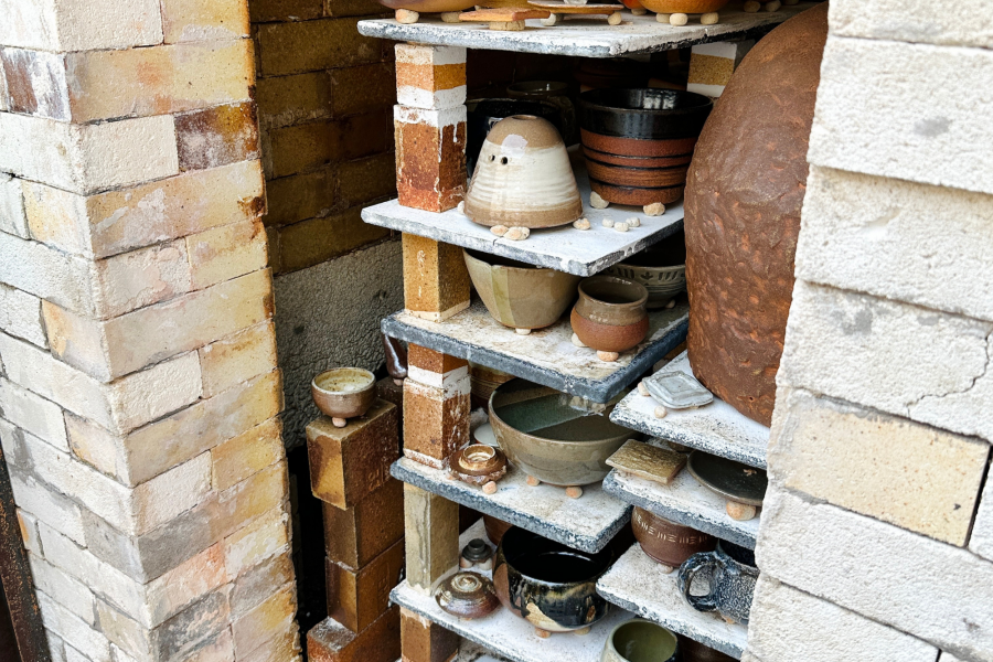A close-up view of a wood-fired kiln filled with handmade ceramic pieces stacked on shelves, showing varied glazes and textures from the firing process.