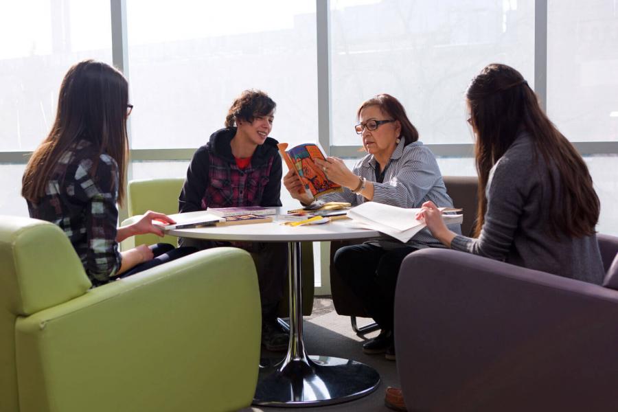 Four people sit around a circular table and look at books together.