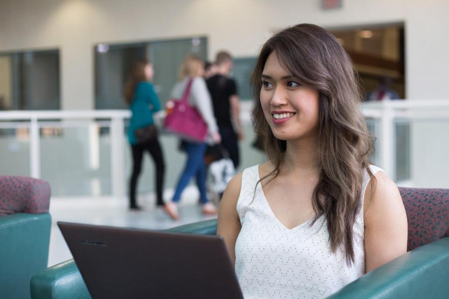 A student seated in a chair works on a laptop.