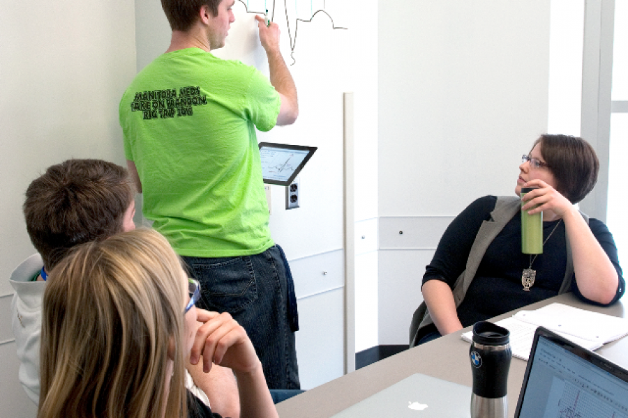 three students are seated and listening to a fourth student explain a diagram.