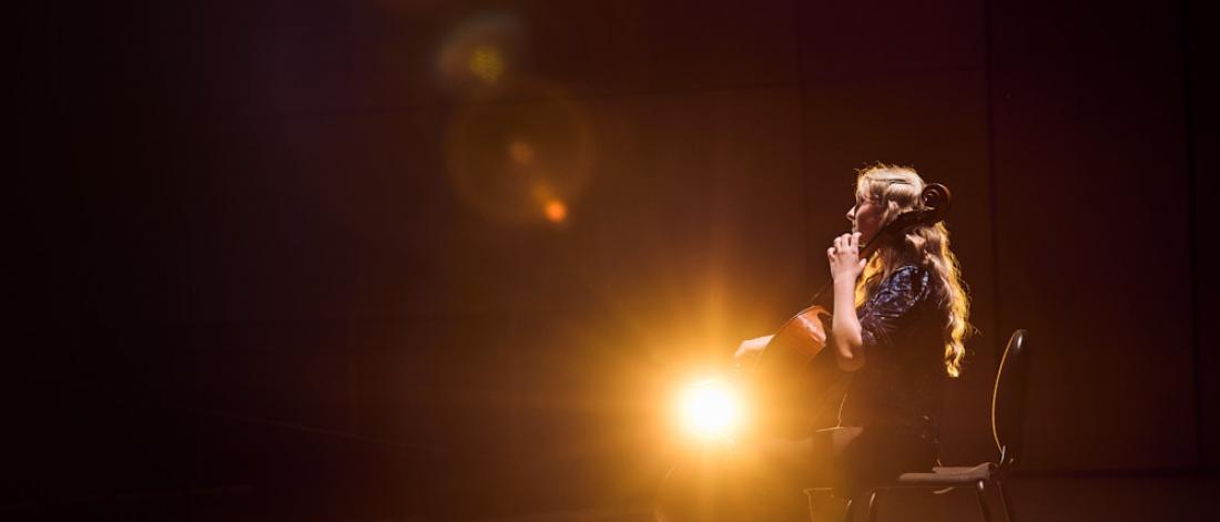 woman illuminated by orange light onstage playing the cello