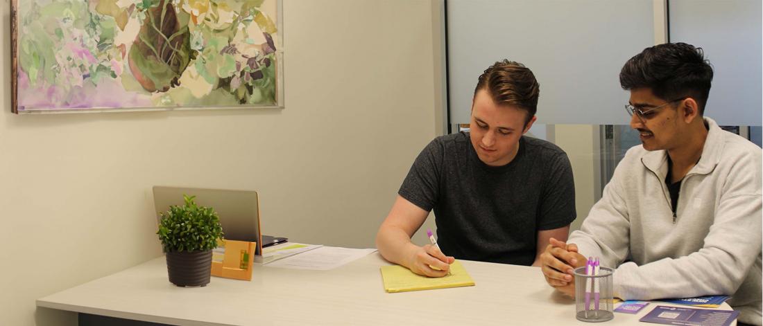 Two student advisors sitting at a table looking at a piece of yellow paper while one of them writes on it.